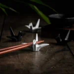 Zwei weiße und zwei schwarze Hashioki Essstäbchenhalter in Kranichform. Auf einem liegt ein paar Sushi Stäbchen.