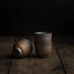 Drei goldschimmernde, japanische Teetassen aus Keramik auf einem hölzernen Untergrund.