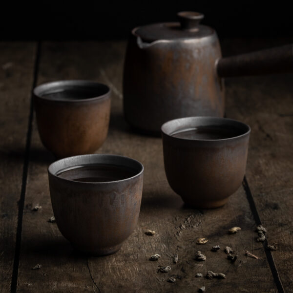 Drei mit Tee befüllte japanische Teetassen aus Keramik vor einer Kyusu-Teekanne.
