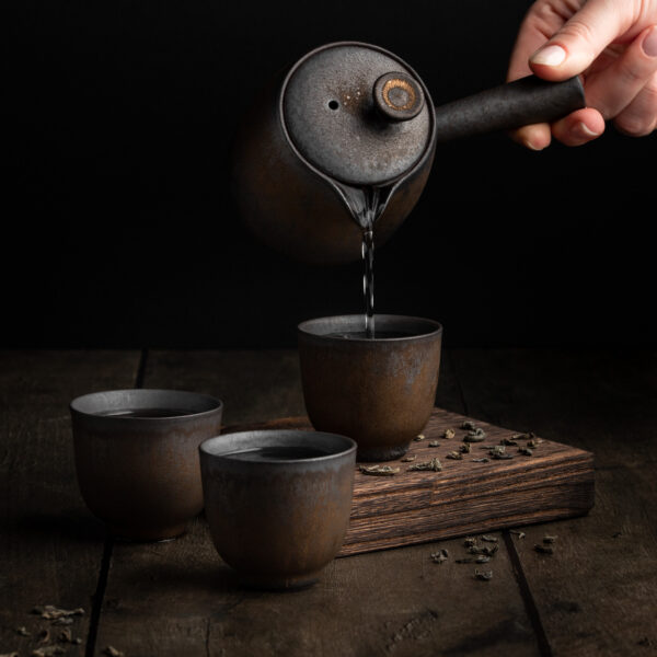 Aus der traditionell, japanischen Teekanne Kyusu wird grüner Tee in kleine Teetassen aus Keramik gegossen.