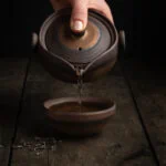 Aus der traditionellen Gaiwan Teekanne aus Keramik wird der grüne Tee in eine Tasse gegossen.