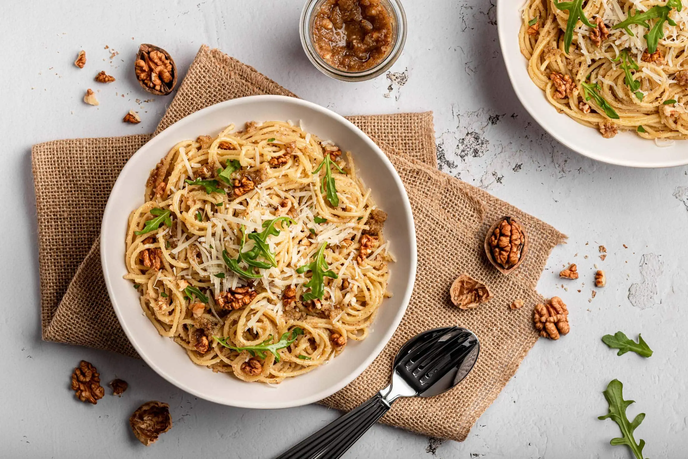 Italienisches Walnusspesto mit Parmesan und gehacken Walnüssen serviert zu Pasta auf zwei Tellern.