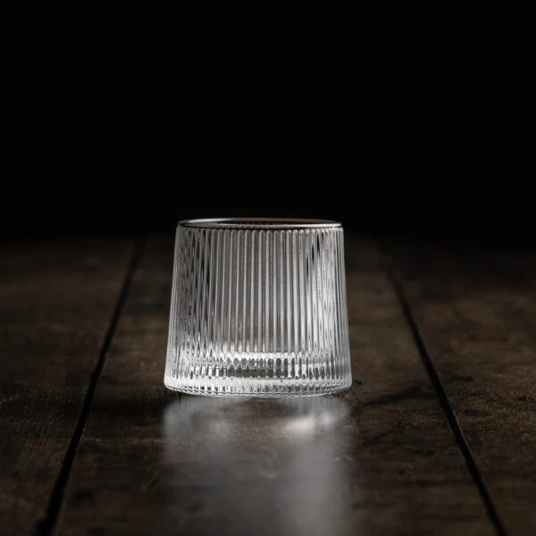 Ein origineller Whisky-Tumbler mit geradlinigen Zierschliff auf einem Holztisch.