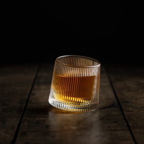 Ein rotierendes Wackelglas gefüllt mit Whisky steht auf einem Holztisch.