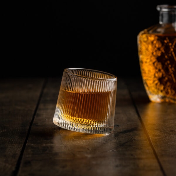 Ein besonderes Whiskyglas mit rundem Boden und edlen Zierschliff gefüllt mit Whisky vor einer Flasche.