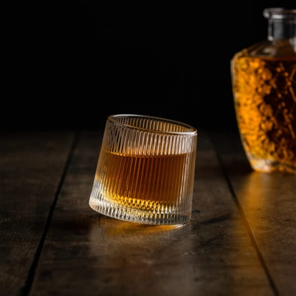 Ein besonderes Whiskyglas mit rundem Boden und edlen Zierschliff gefüllt mit Whisky vor einer Flasche.
