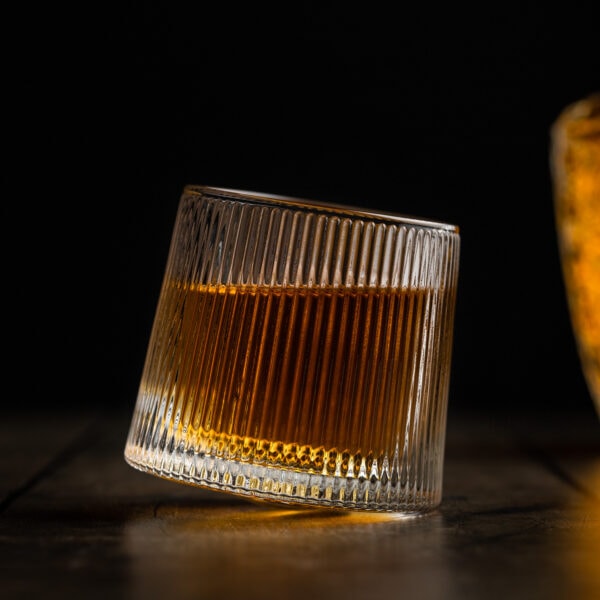 Ein besonderer Whisky-Tumbler mit rundem Boden gefüllt mit Whisky auf einem Holztisch.