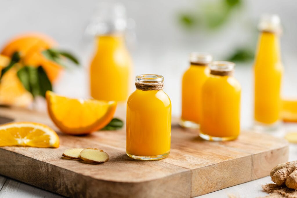 Mehrere Ingwer-Orangen Shots auf einem Holzbrett in Flaschen abgefüllt.