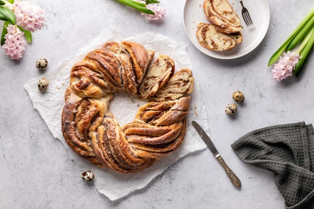 Ein angeschnittener saftiger Hefezopf mit Marzipan-Nuss-Füllung auf einem weißen Untergrund.