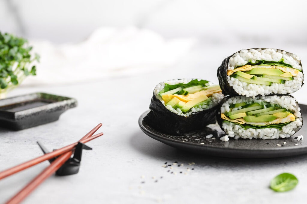 Drei halbierte Onigirazu mit Avocado auf einem Teller.