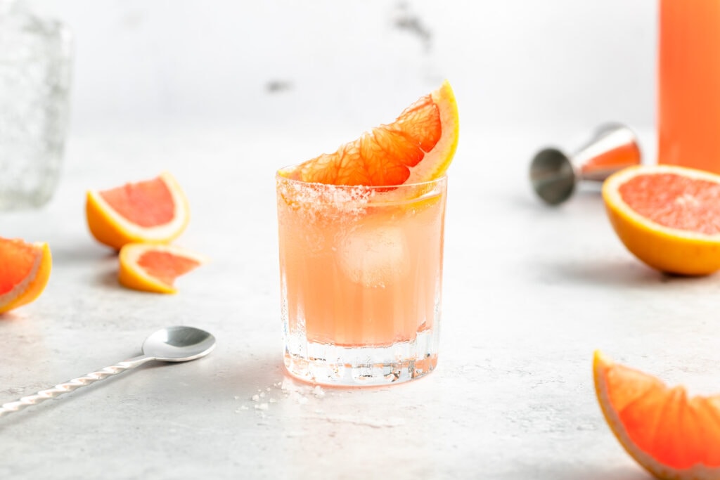 Pink Paloma mit Tequila und Grapefruitlimonade im Glas, garniert mit einer Grapefruitscheibe und Salzrand.