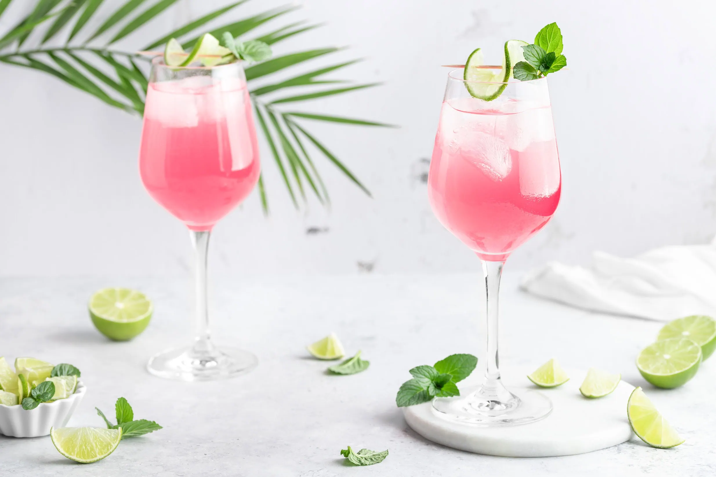 Zwei rosafarbene Sarti Spritz in Weingläsern, garniert sind die Aperitifs einer Limettenscheibe.