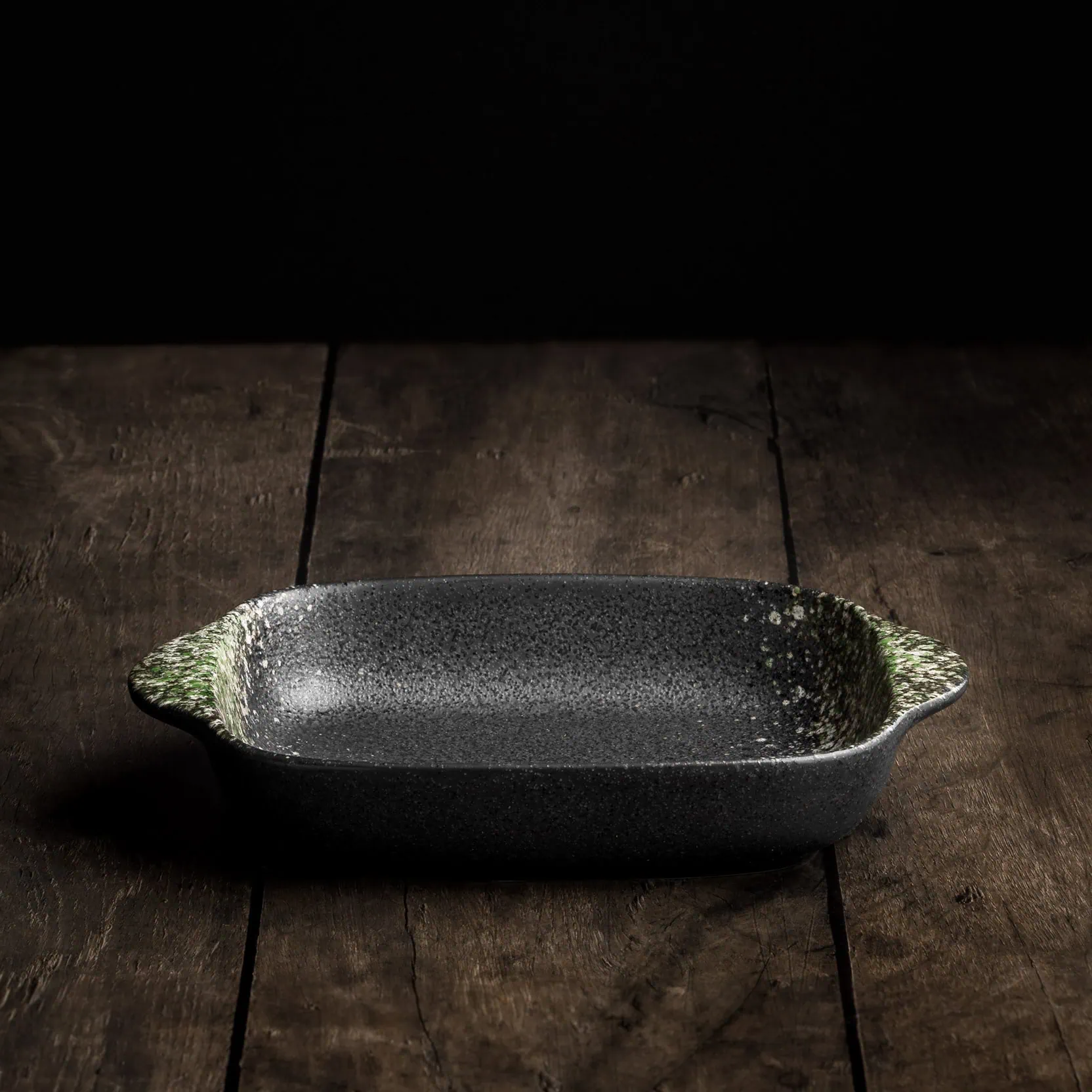 Eine kleine Auflaufform aus Keramik in rechteckiger Form mit zwei abgerundeten Griffen in den Farben schwarz und grün.