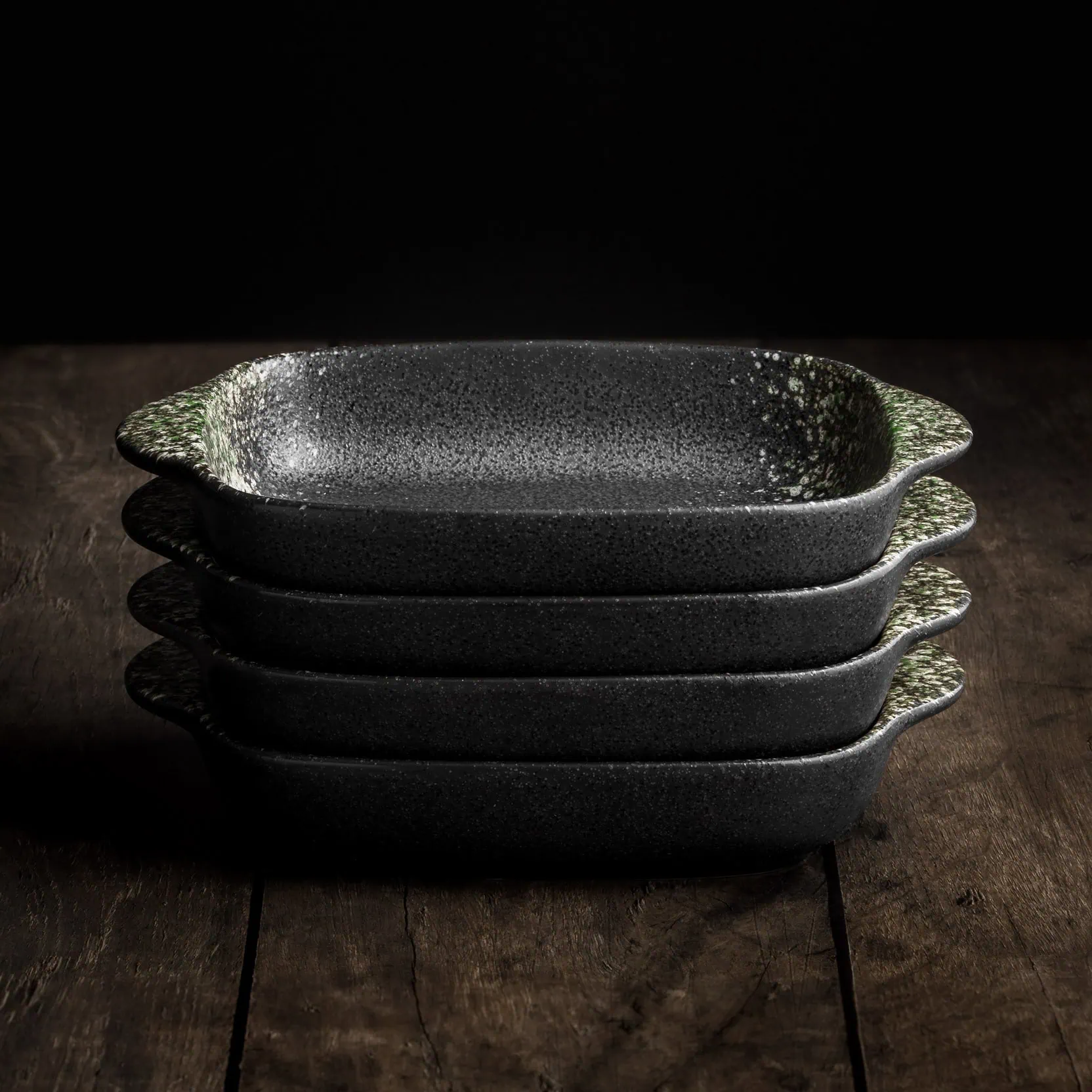 Vier aufeinandergestapelte, rechteckige Mini-Auflaufformen aus hochwertiger Keramik in Schwarz mit grünen Sprenkeln.