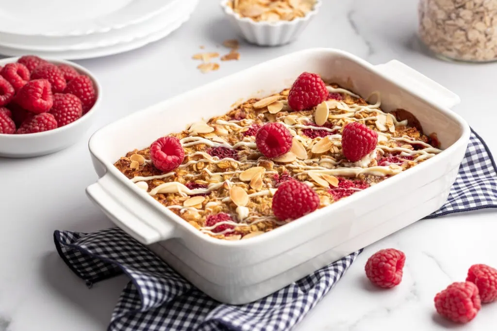 Baked Oatmeal mit Himbeeren, Banane & weißer Schokolade in einer weißen Auflaufform.