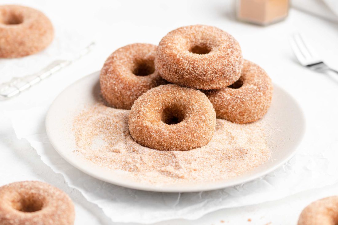 Frisch gebackene Apfel-Donuts werden auf einem Teller in Zimt und Zucker gewälzt.