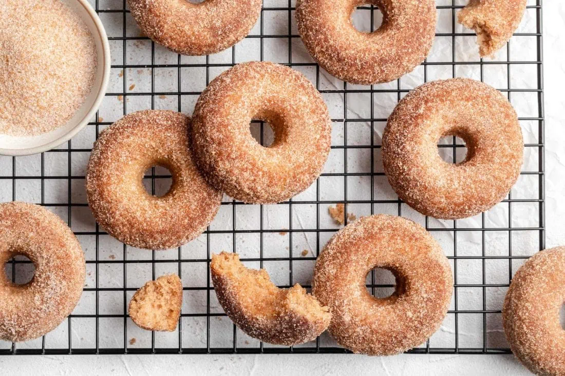 Apfel-Donuts aus dem Ofen mit einem Topping aus Zimt und Zucker liegen auf einem Abkühlgitter.
