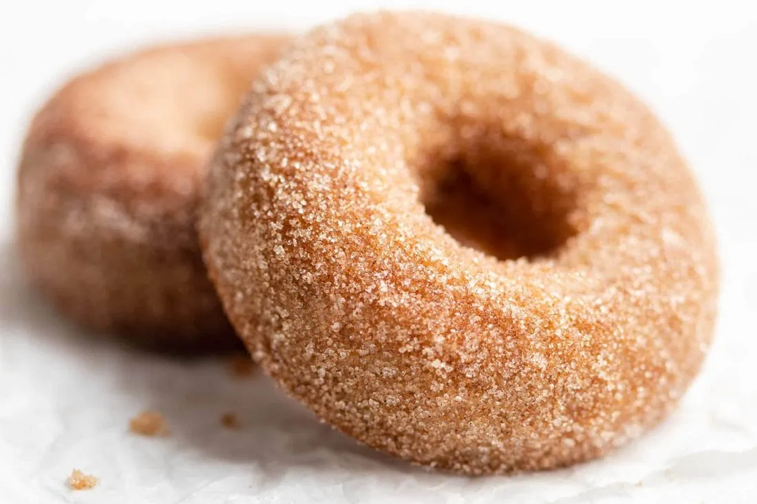 Zwei fluffige Apfel-Donuts mit einem Topping aus Zimt und Zucker.