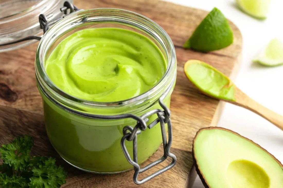 Avocado-Limetten-Mayonnaise ohne Ei abgefüllt in einem Bügelverschlussglas auf einem Holzbrett.