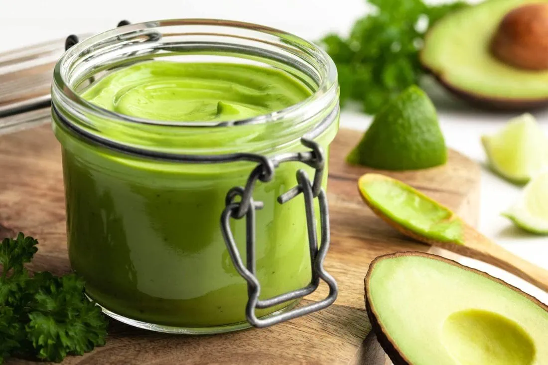 Avocado-Limetten-Mayonnaise umgeben von den zugehörigen Zutaten wie Avocado, Limetten und Petersilie.Avocado-Limetten-Mayonnaise umgeben von den zugehörigen Zutaten wie Avocado, Limetten und Petersilie.