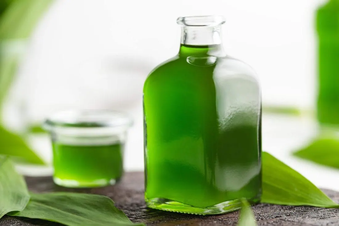 Würziges Bärlauchöl aus Rapsöl in einer Flasche. Daneben liegen frische Bärlauchblätter.