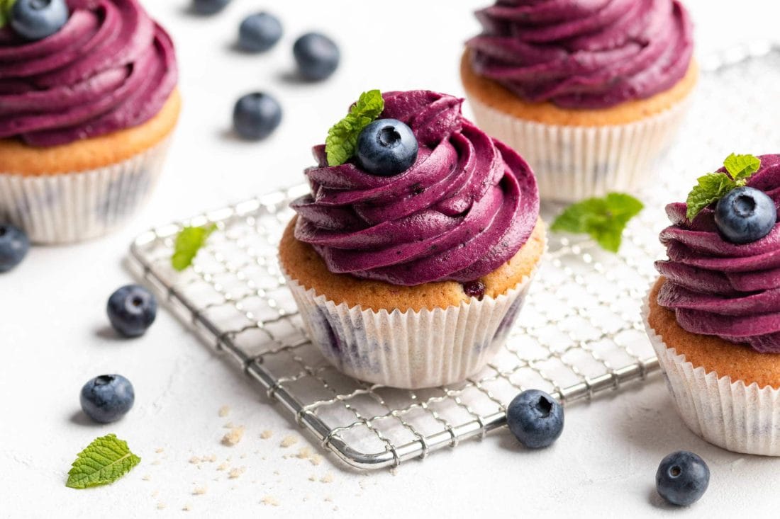 Blaubeer-Cupcakes, getoppt mit einem lilafarbenen Frosting auf einem Kuchengitter.