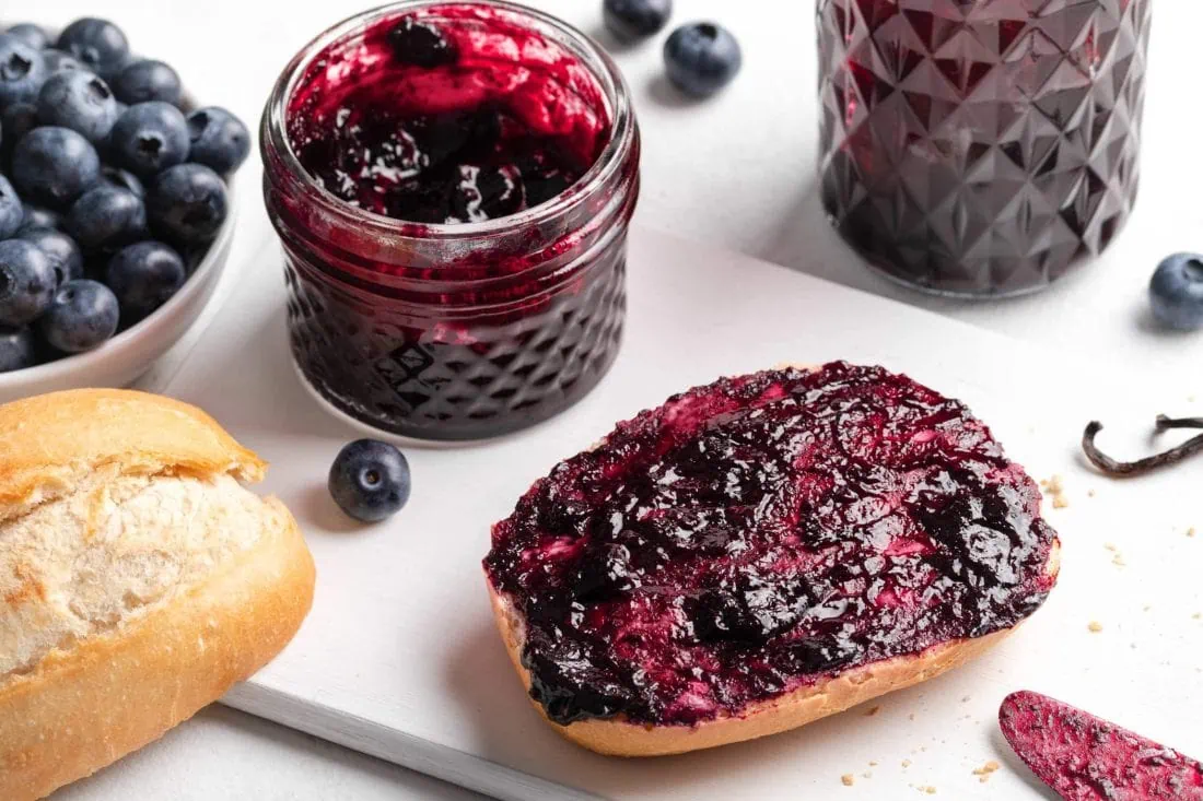 Blaubeermarmelade mit Vanille auf einem aufgeschnittenen Brötchen.