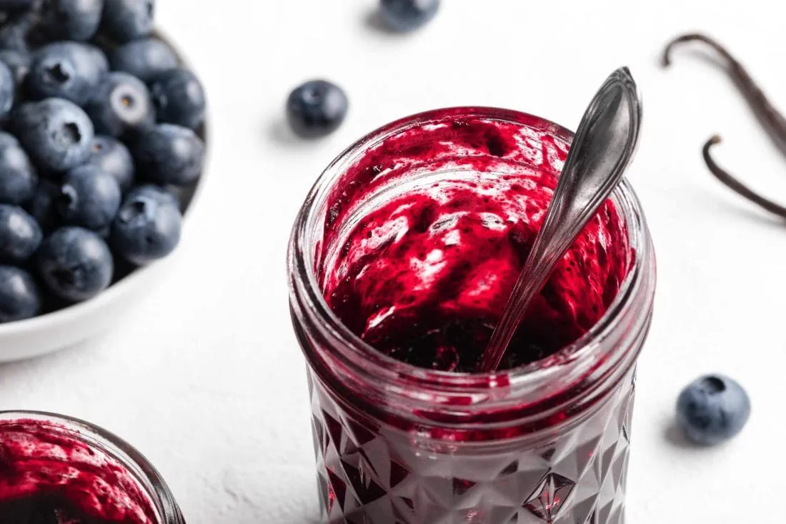 Fruchtige Blaubeermarmelade mit Vanille in einem Glas mit Löffel darin.