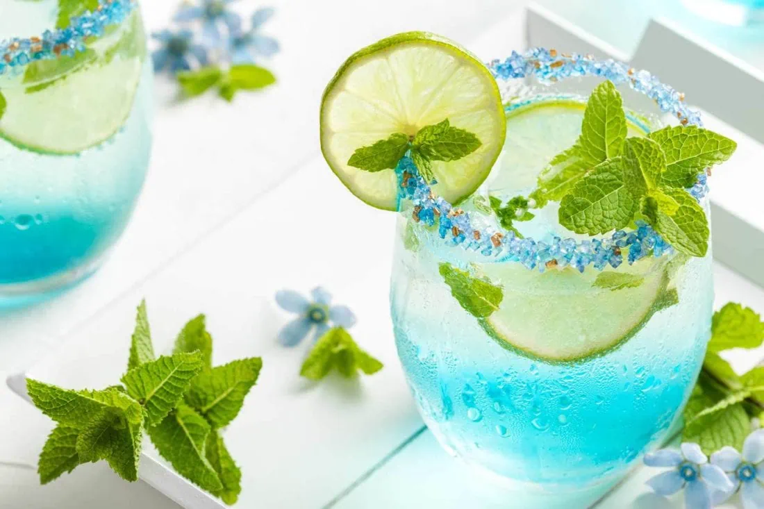 Blauer Hugo mit Blue Curaçao garniert mit frischer Minze und Limette.