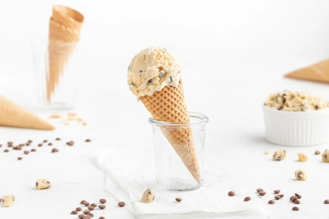 Eine große Kugel Cookie Dough Eis in einer Eiswaffel. Neben der Waffel liegen kleine Keksteigstücke und Chocolate Chips.