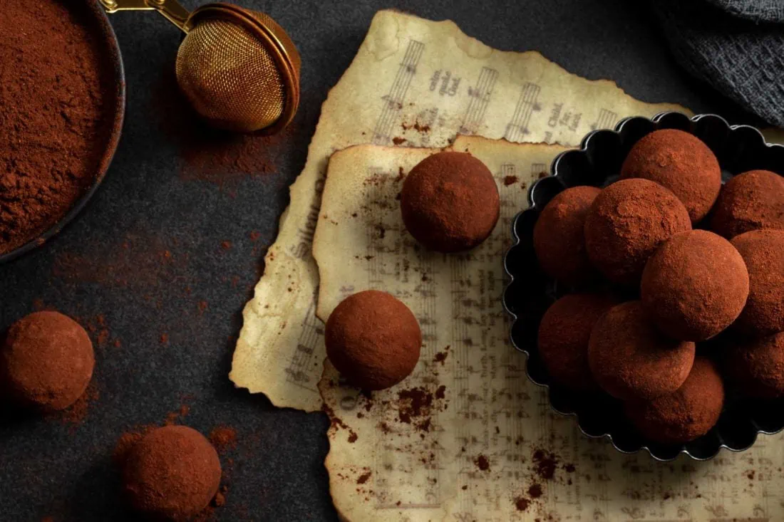 Cranberry-Lebkuchen-Pralinen mit Backkakao in einem dunklen Schälchen, welches auf Notenblättern mit Weihnachtsliedern steht.