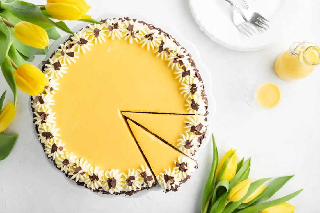 Der cremige Käsekuchen mit Eierlikör von oben fotografiert. Daneben stehen gelbe Tulpen und eine Flasche mit Eierlikör.