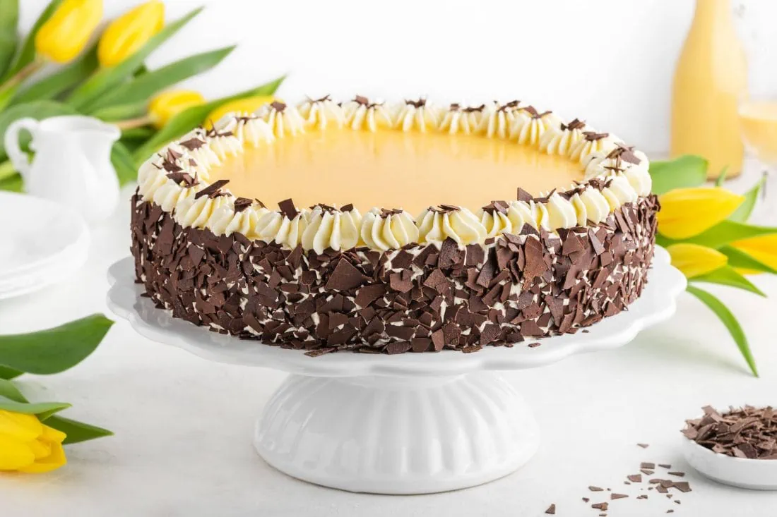 Cremiger Eierlikör-Käsekuchen mit Schokoraspeln serviert auf einer weißen Tortenplatte.