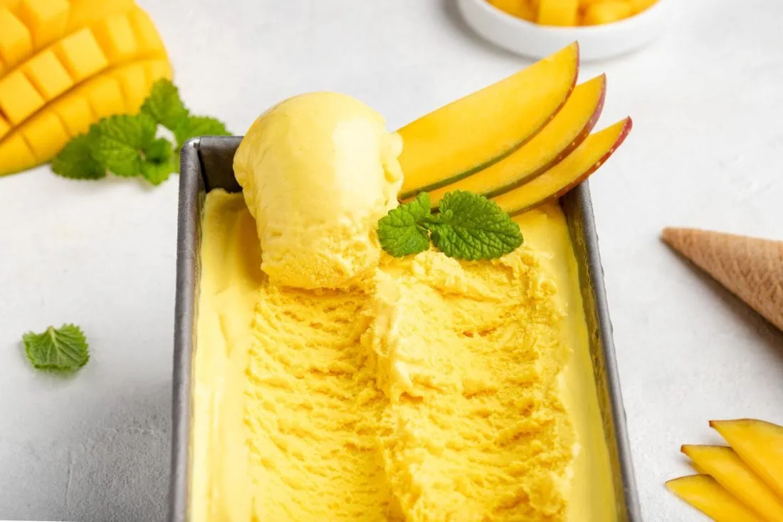 Das Mangoeis in einer rechteckigen Form mit einer Eiskugel darauf und frischer Mango.