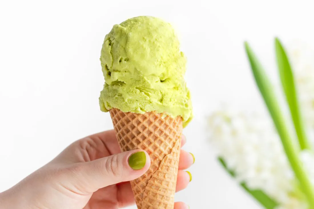 Eine Hand hält eine Eiswaffel in der Hand, in der eine grüne Kugel Pistazieneis ist.
