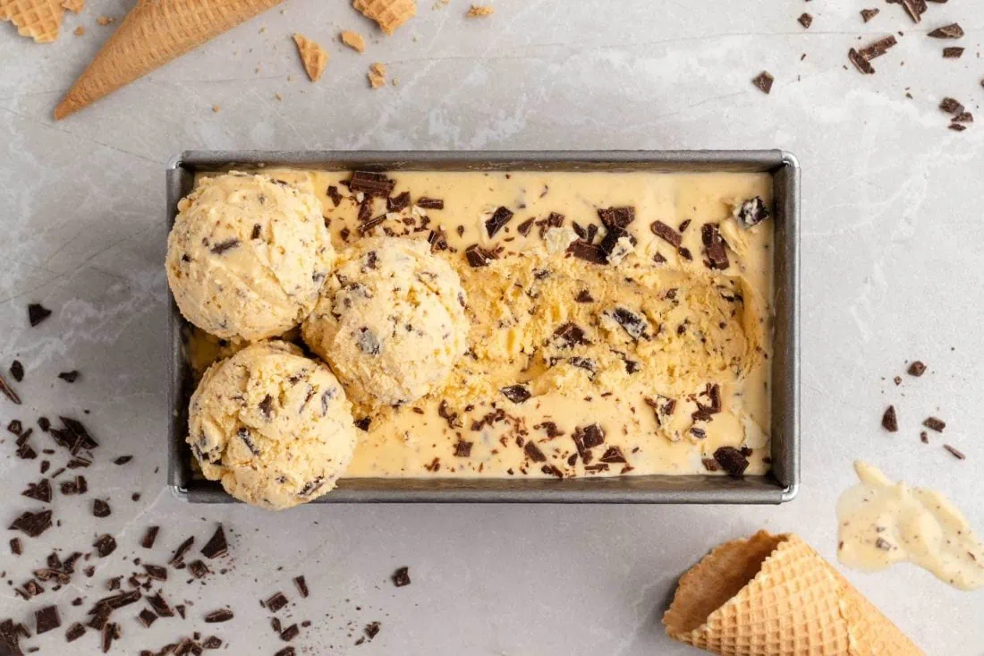 Eierlikör-Eis in einer eckigen Form. Daneben liegen Eiswaffeln und Schokoladenstücke.