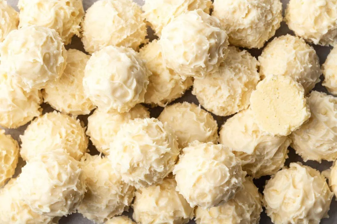 Nahaufnahme von mehreren Eierlikör-Pralinen überzogen mit weißer Schokolade. Eine Praline ist angebissen.
