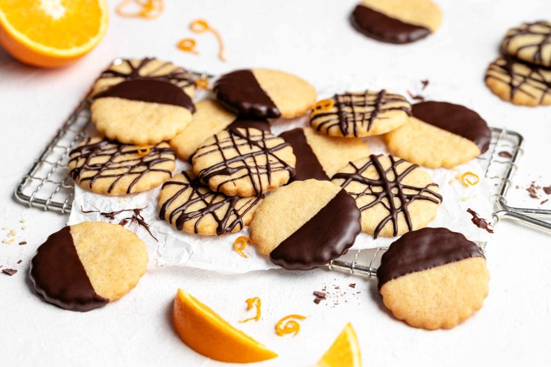 Einfache Orangenplätzchen mit Schokolade liegen neben einer in Stücke geschnittenen Orange auf einem Kuchengitter.