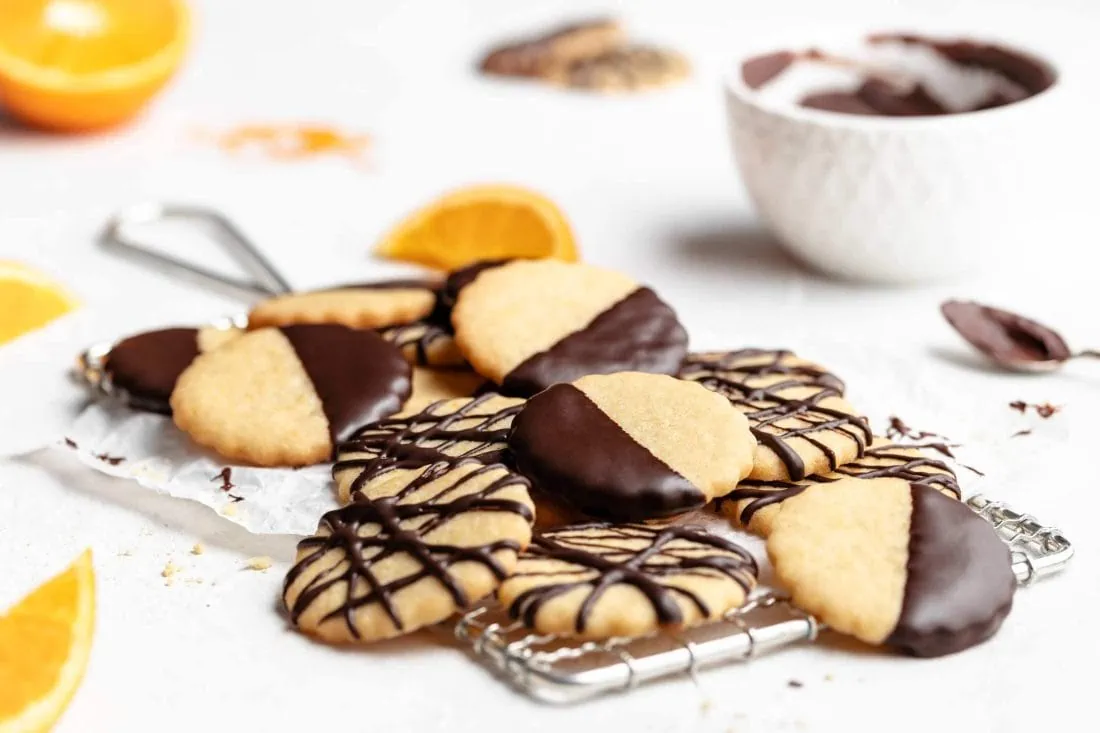 Einfache Orangenplätzchen auf einem Gitter. Daneben steht eine Schüssel mit geschmolzener Schokolade.