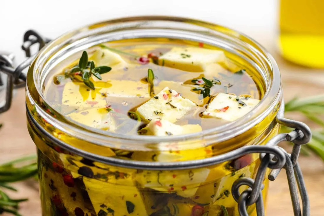 Eingelegter Schafskäse in Olivenöl mit Thymian, Rosmarin, Chili und roten und schwarzen Pfefferkörnern.