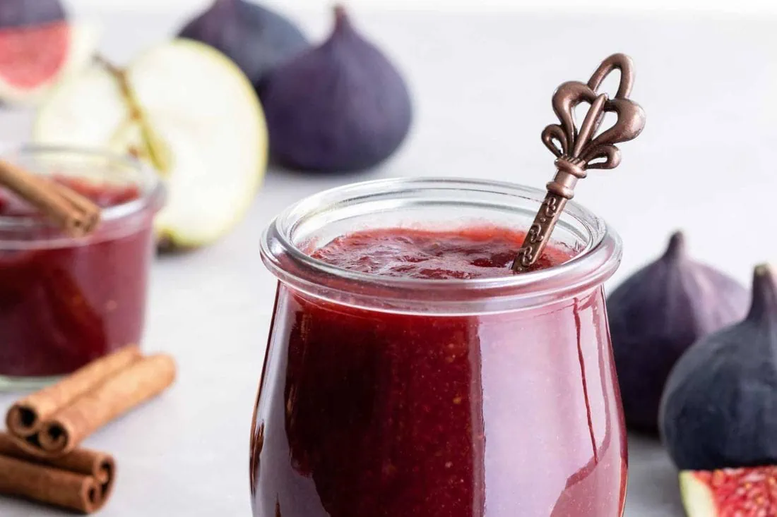 Feigenmarmelade mit Apfel und Zimt in einem Glas mit Löffel. Daneben die dazugehörigen Zutaten.