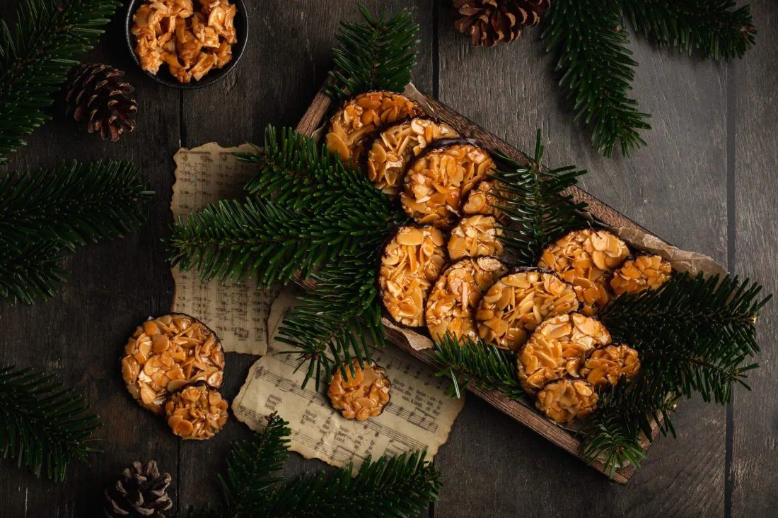 Mehrere Florentiner Kekse in verschiedenen Größen in einer Holzschale mit frischen Tannenzweigen als Dekoration.