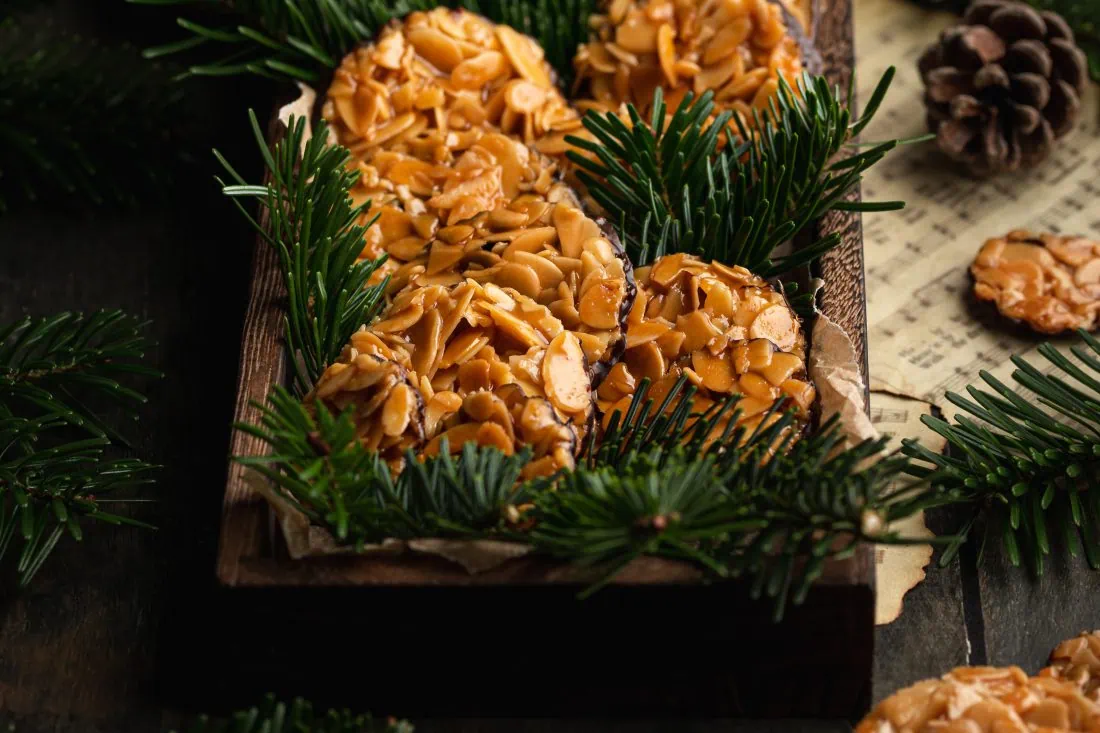 Florentiner Plätzchen, ein Gebäck aus karamellisierten Mandeln mit einem dünnen Schokoladenboden, auf einer Holzplatte.