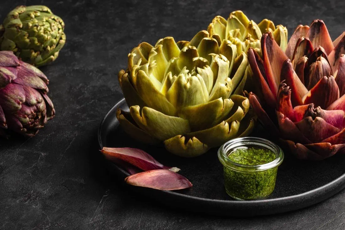 Frische Artischocken gekocht und mit einer Kräuter-Vinaigrette auf einem Teller serviert.