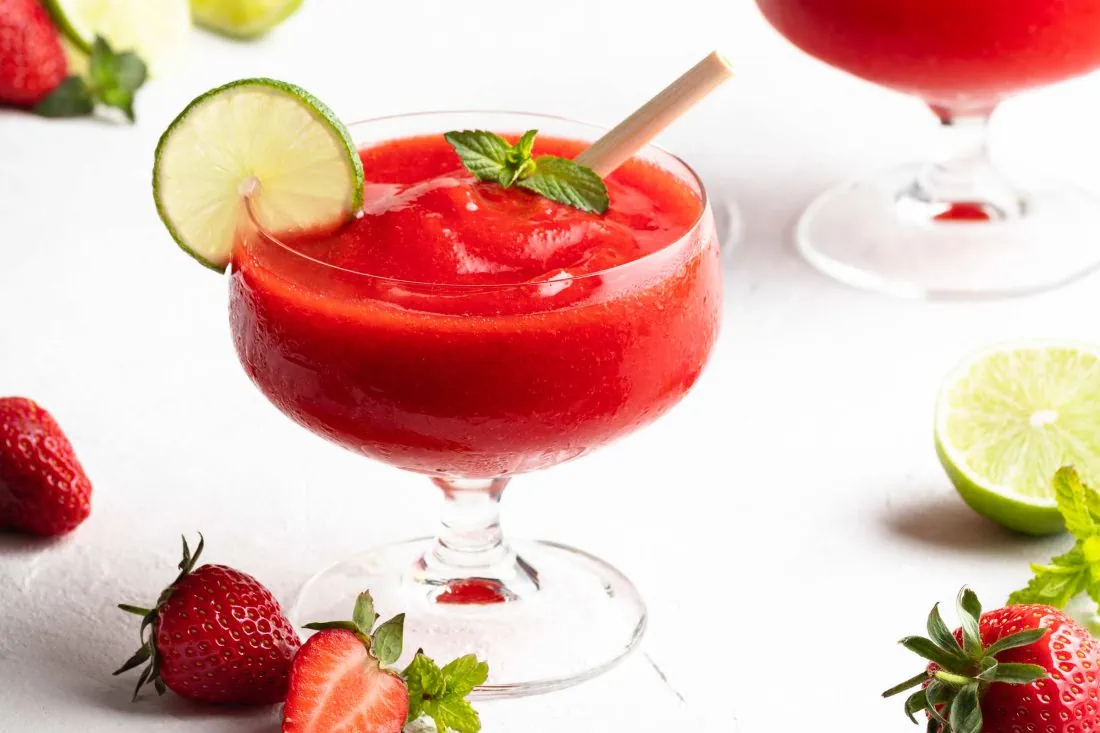 Frozen Erdbeer Daiquiri in einem Glas mit Strohhalm und einer Limettenscheibe am Rand.