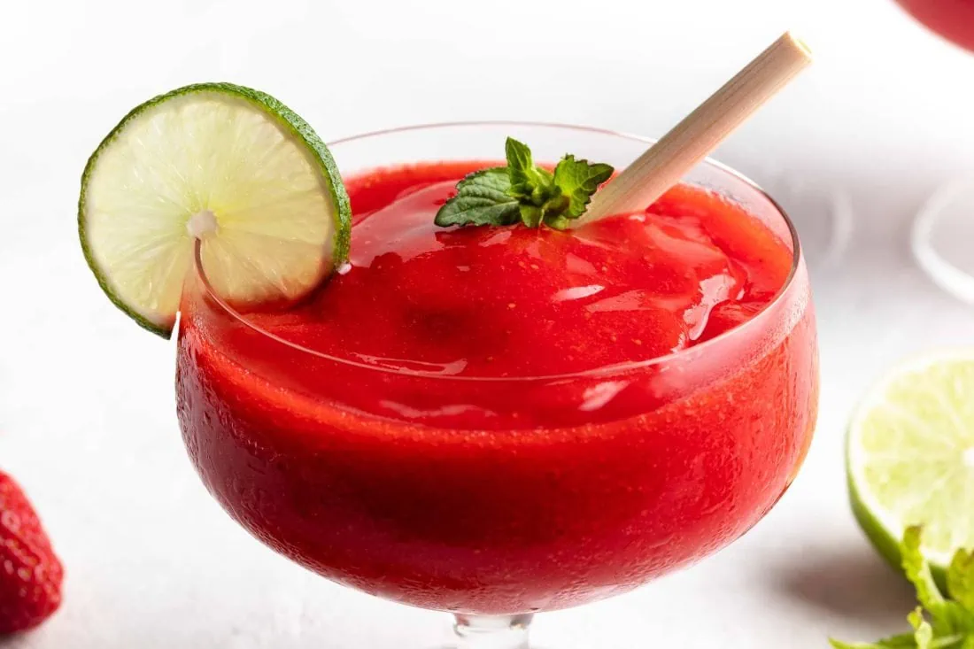 Frozen Erdbeer Daiquiri mit der Konsistenz von Slusheis in einem Glas mit Stiel garniert mit frischer Minze.