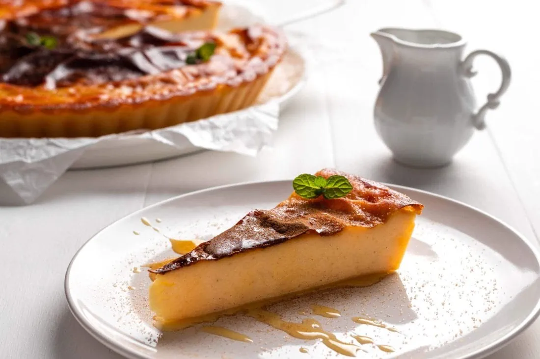 Ein Stück griechische Galatopita auf einem Kuchenteller bestreut mit Zimt, Zucker und Honig.