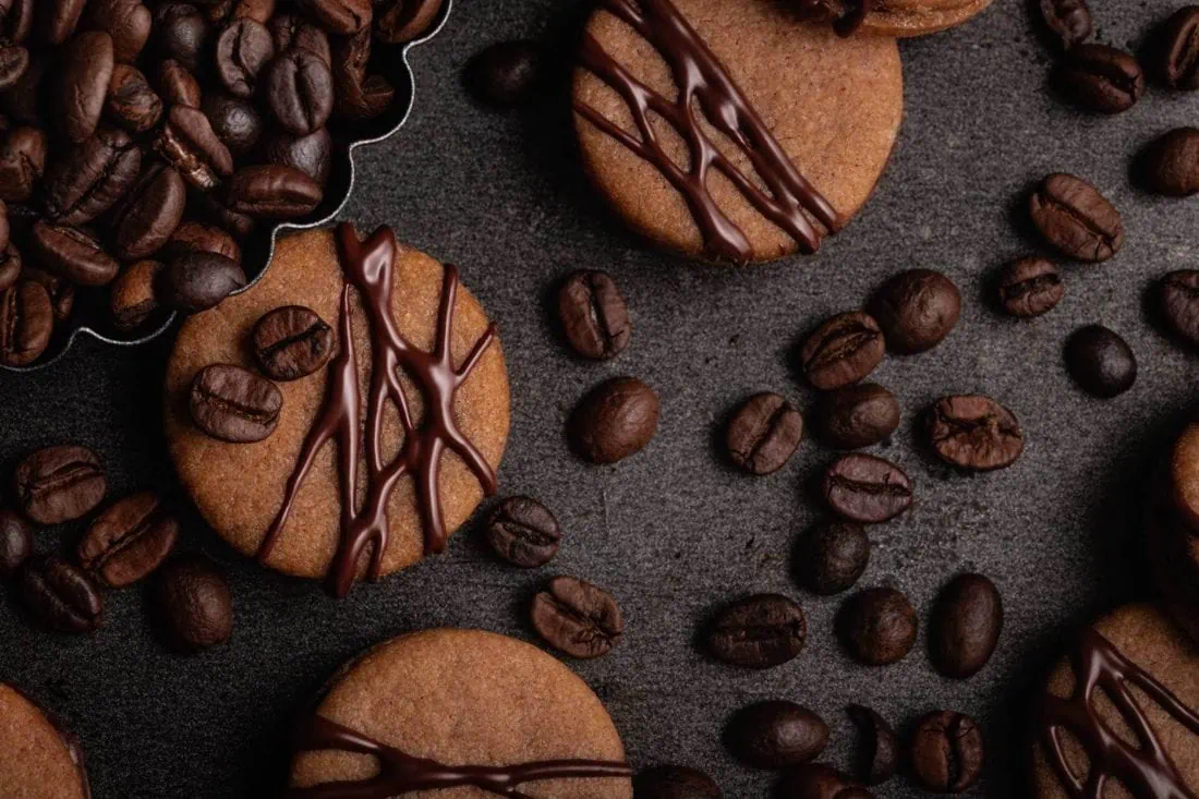 Mehrere Kaffeeplätzchen verziert mit Zartbitterschokolade und ganze Kaffeebohnen liegen nebeneinander.