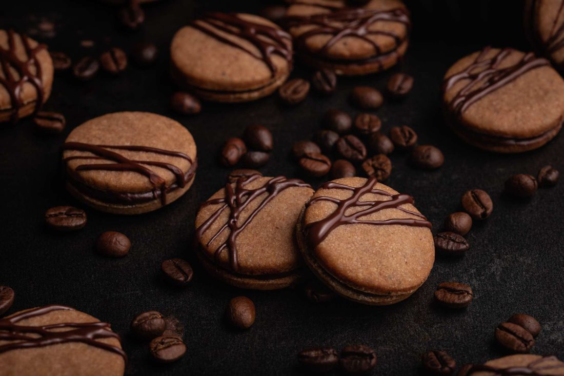 Kaffee Plätzchen mit Kakao verziert mit Zartbitterschokolade und einer Füllung aus einer Kaffeeganache liegen neben einzelnen Kaffeebohnen.
