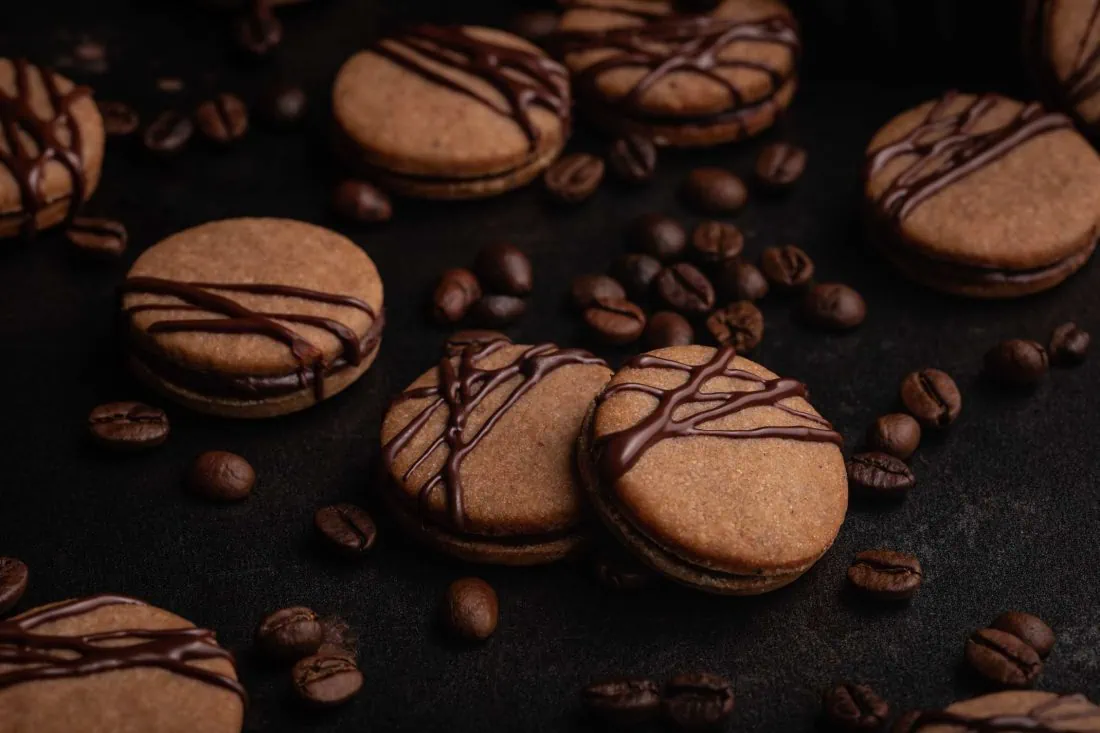Kaffee Plätzchen mit Kakao verziert mit Zartbitterschokolade und einer Füllung aus einer Kaffeeganache liegen neben einzelnen Kaffeebohnen.